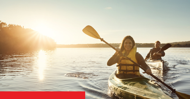 Zwei Menschen im Kajak bei Sonnenuntergang auf einem ruhigen Gewässer, beide tragen Schwimmwesten.