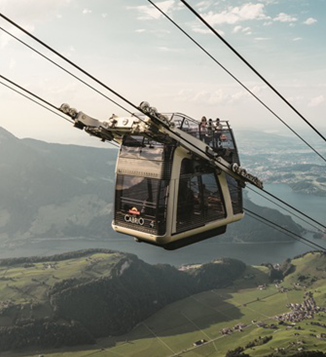 Die CabriO-Seilbahn am Stanserhorn mit Fahrgästen auf dem offenen Oberdeck vor See- und Bergkulisse.