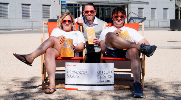 Drei Personen im Freien mit Sonnenbrillen, Popcorn und einem Scheck für das Solarkino.