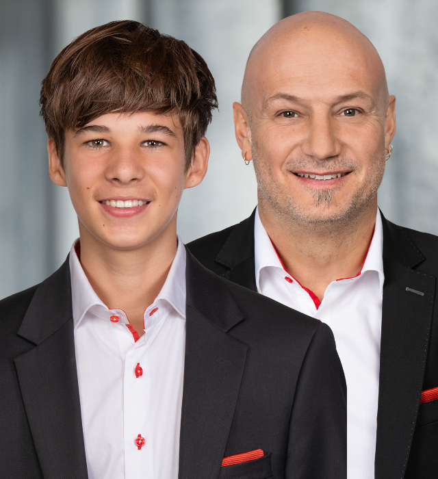 Zwei Personen in eleganter Kleidung mit schwarzem Sakko und weissen Hemden mit roten Akzenten.