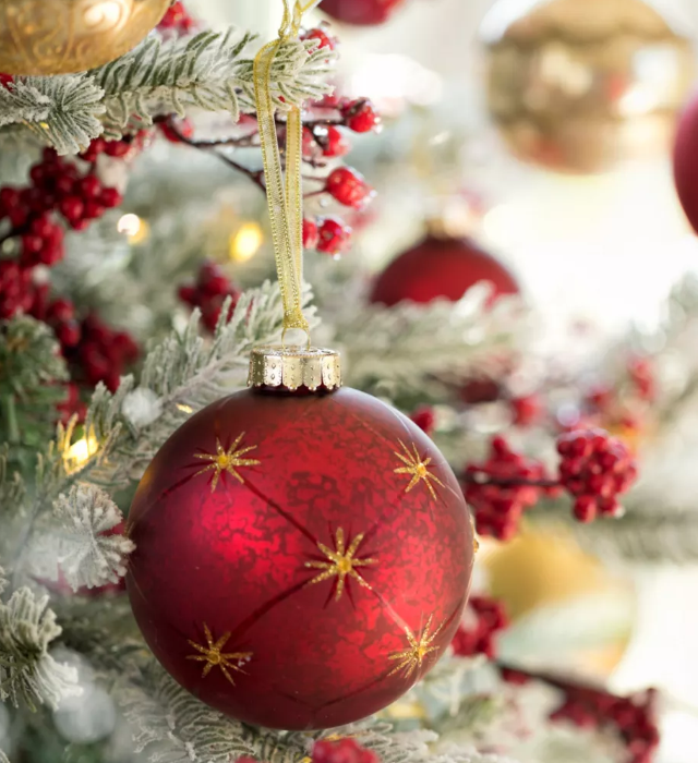 Dekorierte Weihnachtsbaumkugeln in Rot und Gold an einem geschmückten Weihnachtsbaum.