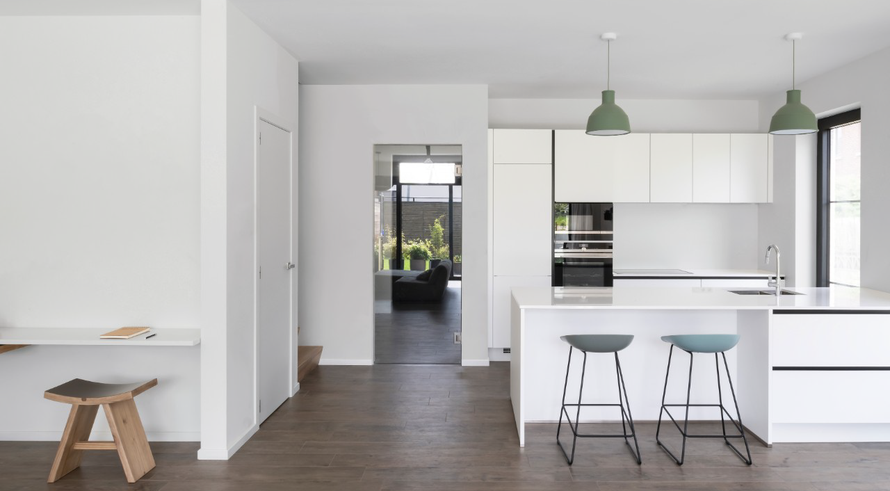 Helle, moderne Küche mit Kochinsel, zwei Barhockern und minimalistischem Wohnbereich im Hintergrund.