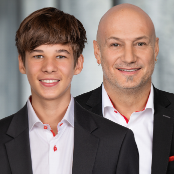 Zwei Personen in eleganter Kleidung mit schwarzem Sakko und weissen Hemden mit roten Akzenten.