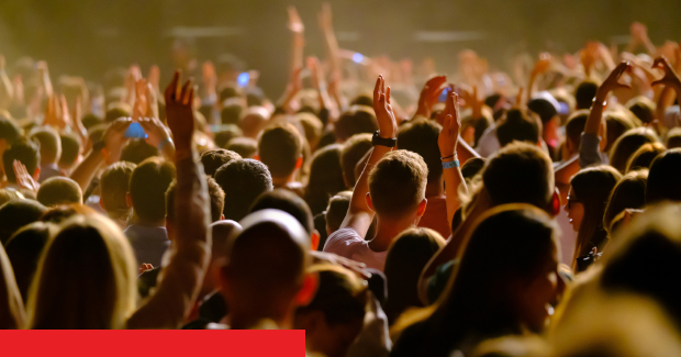 Menschenmenge in einem Live-Konzert, die Hände heben und feiern, bei schwachem Licht.