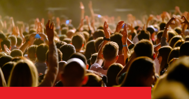 Menschenmenge in einem Live-Konzert, die Hände heben und feiern, bei schwachem Licht.