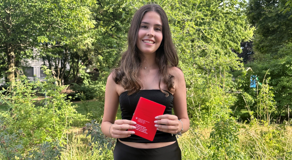 Junge Frau im Freien hält den Lehranschluss in der Hand, umgeben von grüner Natur.