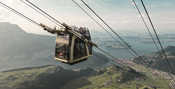 Die CabriO-Seilbahn am Stanserhorn mit Fahrgästen auf dem offenen Oberdeck vor See- und Bergkulisse.